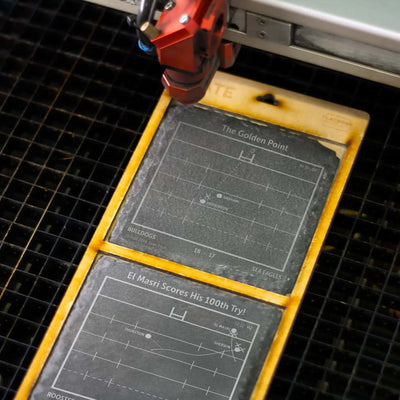 Laser machine engraving NRL playbook coaster design onto slate coaster.